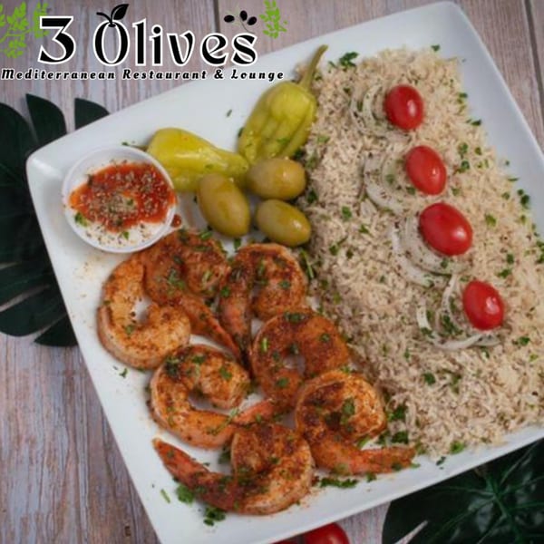 Grilled shrimp with rice, tomatoes, onions, olives, and peppers on a white plate.