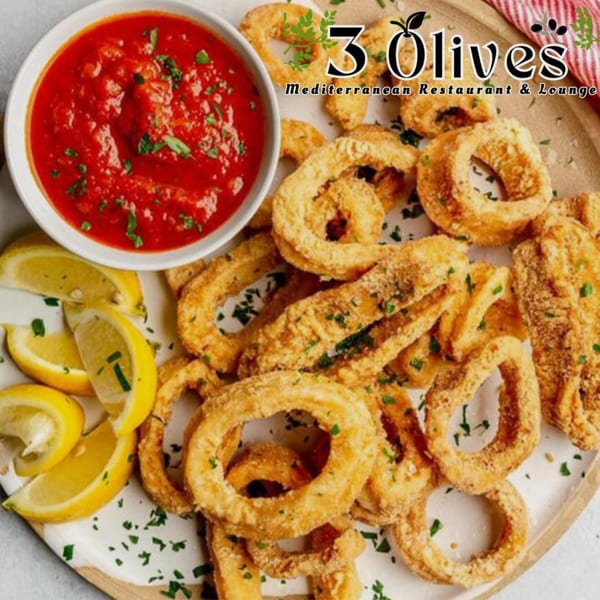 Golden fried calamari rings and strips with lemon wedges and a bowl of red marinara sauce.