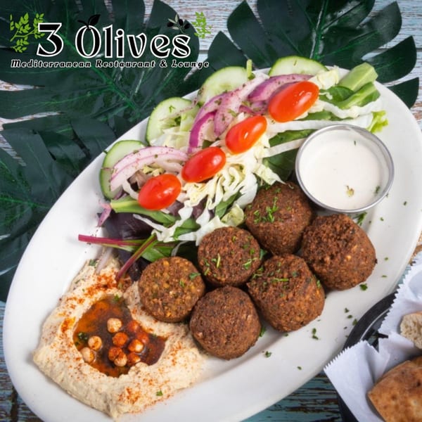 A platter of falafel, hummus, fresh salad with cherry tomatoes, and a side of white sauce.