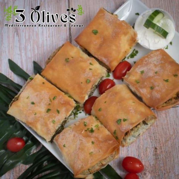 Six golden-brown savory pastries, garnished with cherry tomatoes and a side of cucumber yogurt dip.