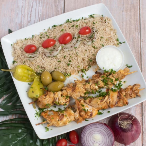 Halal chicken shish tawook with rice, tomatoes, onions, peppers, olives, and a white sauce.