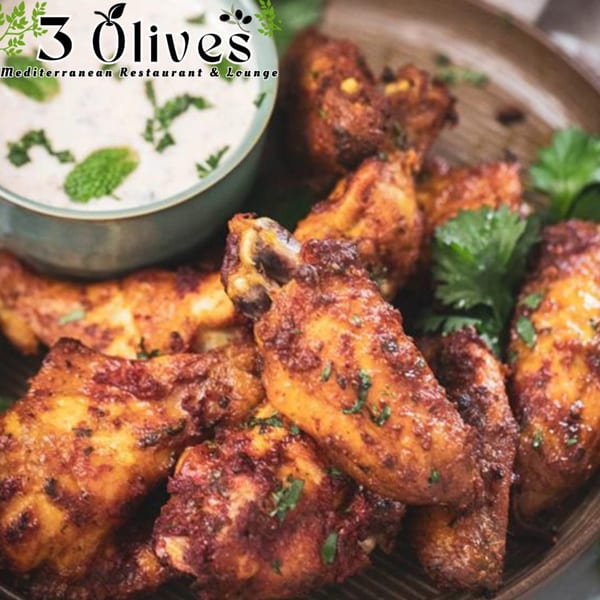 Platter of crispy, spiced chicken wings with a side of creamy dip garnished with mint.