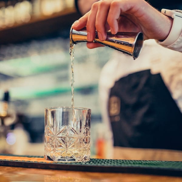 A bartender pours a drink from a jigger into a patterned glass at 3 Olives Mediterranean Grill & Lounge.