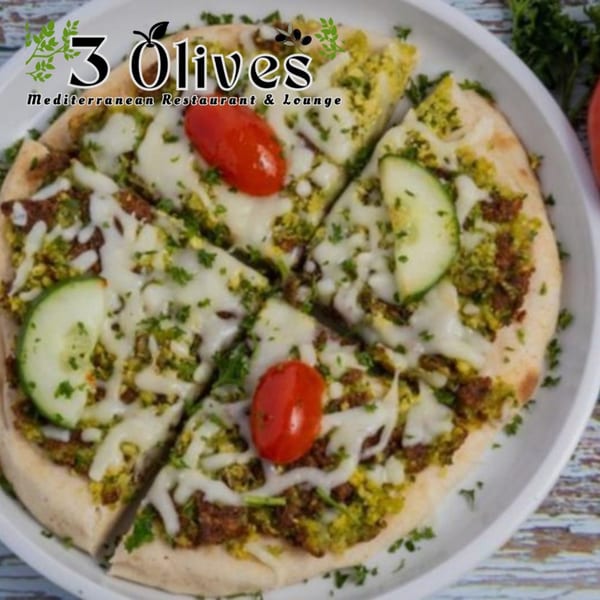 A sliced Mediterranean flatbread pizza with pesto, cheese, ground meat, zucchini, and cherry tomatoes.